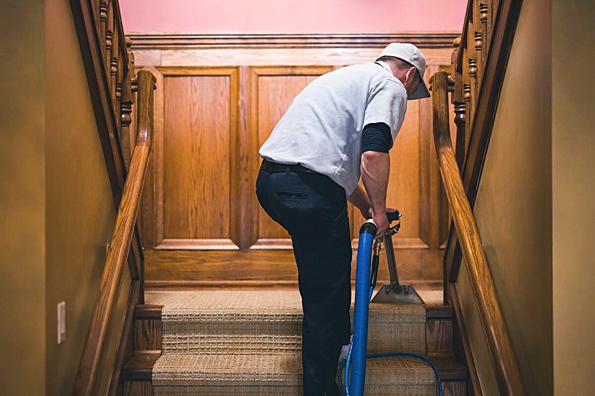 Technician cleaning a carpeted staircase in a wood-panelled building